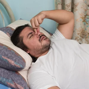 Man squeezing his nose while laying in bed due to sleep apnea and schizophrenia